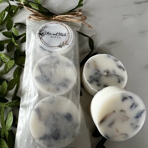 May include: Three white round wax melts with a lavender and white marbled design. The wax melts are packaged in a clear plastic bag with a brown twine bow and a white label that reads "Olive and Hatch Gifts".