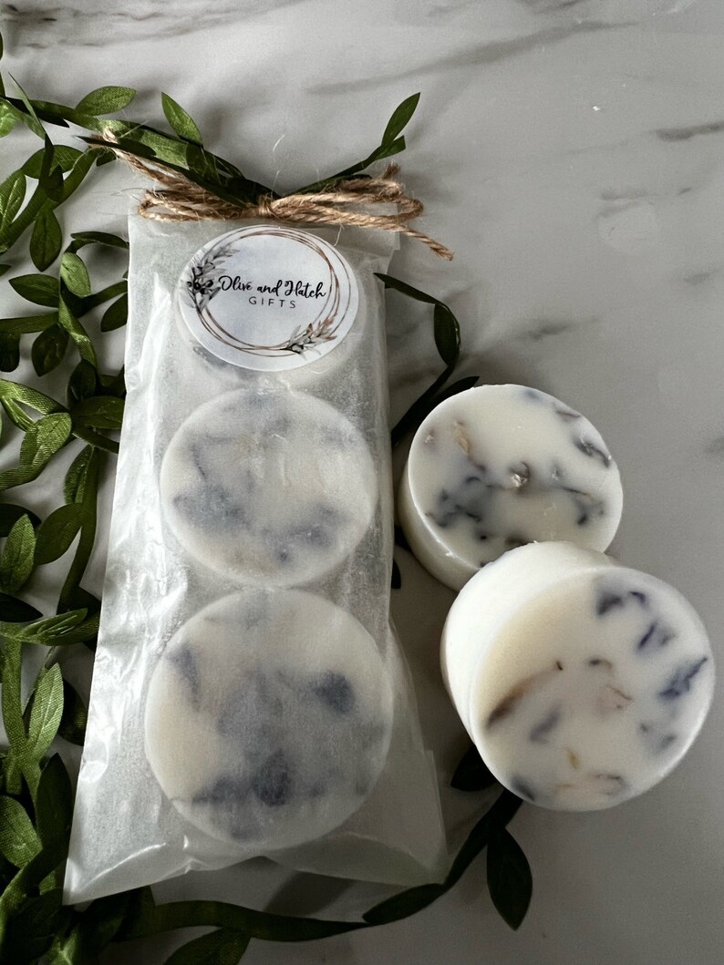May include: Three white round wax melts with a lavender and white marbled design. The wax melts are packaged in a clear plastic bag with a brown twine bow and a white label that reads "Olive and Hatch Gifts".
