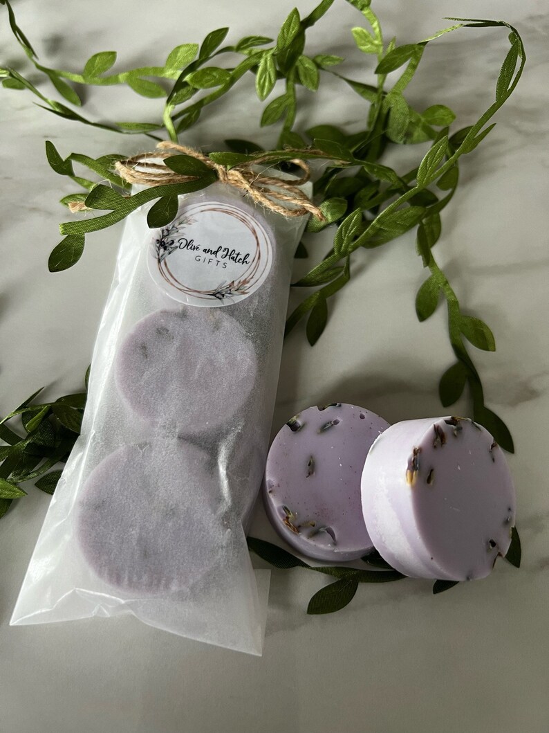 May include: Two lavender-colored bath bombs with dried lavender flowers, packaged in a white paper bag with a brown twine bow and a label that reads "Olive and Hatch Gifts".