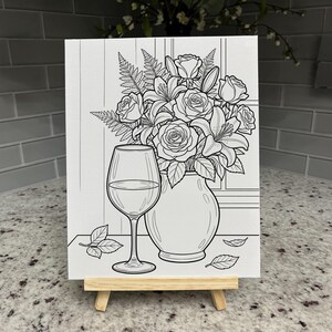 May include: A black and white line art canvas on a wooden easel featuring a bouquet of roses and lilies in a rounded vase next to a stemmed wine glass. The illustration includes scattered leaves on a flat surface with a window pane background.