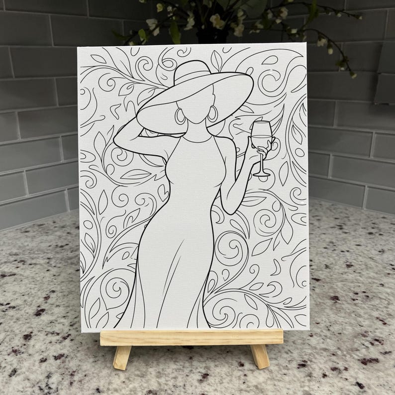 May include: A black and white line art drawing on a rectangular canvas resting on a wooden easel. The illustration depicts a figure wearing a wide-brimmed hat and a dress, holding a wine glass, set against a background of swirling floral patterns.