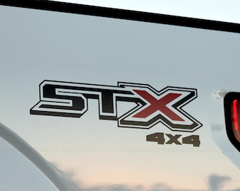 May include: A black and red "STX" emblem with a black "4x4" below it on a white truck tailgate.