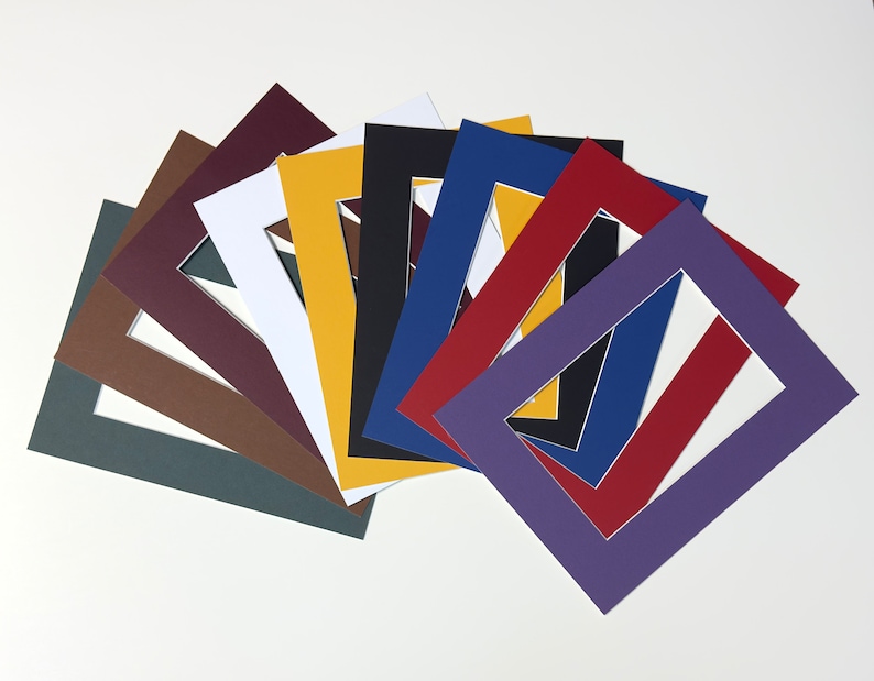 K&ouml;nnte beinhalten: Eine Sammlung rechteckiger Passepartouts aus Papier, die f&auml;cherf&ouml;rmig angeordnet sind. Die Passepartouts weisen eine Vielzahl von Volltonfarben auf, darunter Dunkelgrau, Braun, Kastanienbraun, Wei&szlig;, Gelb, Schwarz, Blau, Rot und Violett, jeweils mit einem mittigen Ausschnitt.