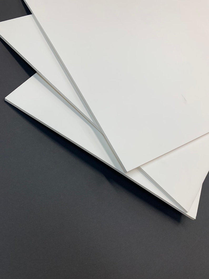 May include: Three white foam core boards stacked on top of each other on a dark gray surface.