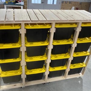 以下が含まれることがあります： 黄色の蓋が付いた黒い収納箱が複数ある木製収納棚。棚は木製で、車輪が付いています。