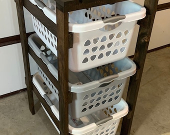 May include: A dark brown wooden laundry rack with four white and grey plastic laundry baskets. The rack has a top shelf and three shelves below.