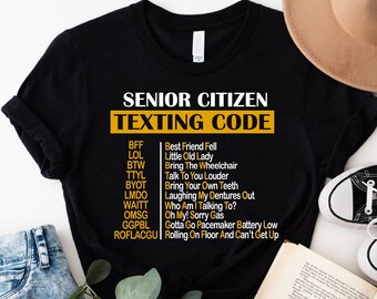 May include: Black t-shirt with a white graphic that says "Senior Citizen Texting Code" and lists common texting abbreviations and their meanings. The abbreviations are in yellow text.
