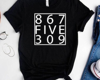 May include: A black short-sleeved t-shirt featuring a white square graphic on the chest. Inside the square, the text reads 8 6 7, FIVE, 3 0 9 in a clean, sans-serif font. The shirt has a crew neckline and is made of a solid black fabric.