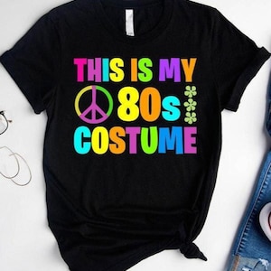 May include: Black t-shirt with the text "This is my 80s Costume" in rainbow colors. A peace sign is included in the design.