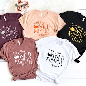 May include: Five t-shirts with the text "Let the Wild Rumpus start!" printed on them. The shirts are in various colors, including maroon, peach, black, and white. The text is in a silver glitter font with a gold crown graphic.