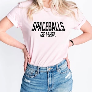 May include: A pink t-shirt with the text "Spaceballs The T-Shirt" in black.