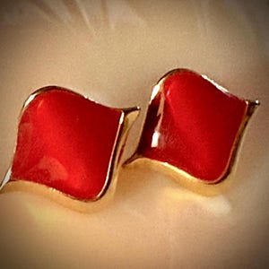 May include: A pair of red, leaf-shaped earrings with a gold-colored trim. The earrings have a glossy finish and a simple, elegant design. The earrings are a bold statement piece.