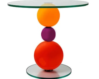 May include: A modern side table with a clear glass top and base. The table's support is composed of three stacked spheres in orange, purple, and red. The table is approximately 20 inches tall.