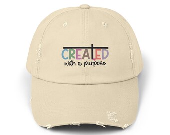 May include: A beige distressed baseball cap with the text "CREATED with a purpose" in colourful letters. The word "CREATED" has a black cross over the "A".