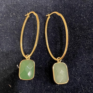 May include: Gold hoop earrings with a green stone pendant. The stone is a rectangular shape with a faceted design.