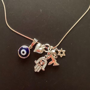 May include: A silver chain necklace with multiple charms, including a blue evil eye, a silver heart, a hamsa hand, a star of David, and a silver angel wing.