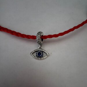 May include: A silver charm with a blue evil eye design. The charm is surrounded by clear crystals and has a silver loop for attaching to a bracelet or necklace.