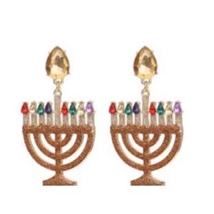 Könnte beinhalten: Ein Paar goldfarbene Chanukka-Menora-Ohrringe. Jeder Ohrring hat ein glitzerndes Menora-Design mit farbigen Edelsteinakzenten und einem großen, tropfenförmigen Gold-Edelstein oben. Die Ohrringe sind zum Hängen konzipiert.