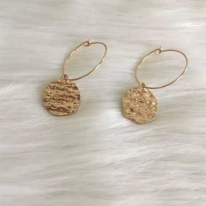 May include: Gold hoop earrings with a textured round pendant. The pendant has a hammered metal look.