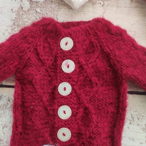 May include: Red knitted baby sweater with white trim and white buttons down the front.