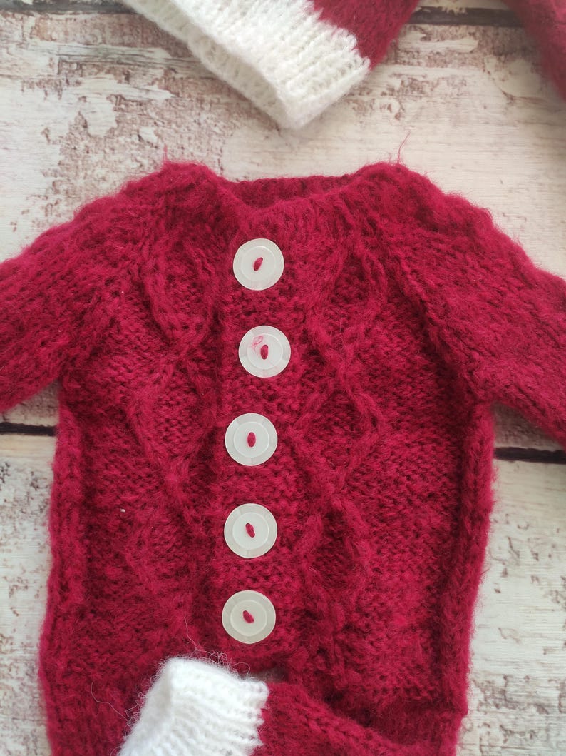 May include: Red knitted baby sweater with white trim and white buttons down the front.