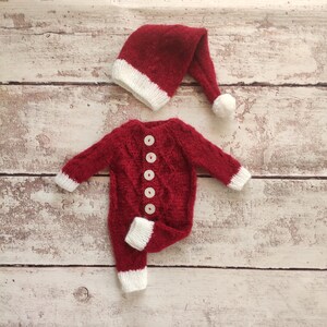 May include: Red knitted baby outfit with white trim and buttons, and a matching red knitted Santa hat with a white pom-pom.