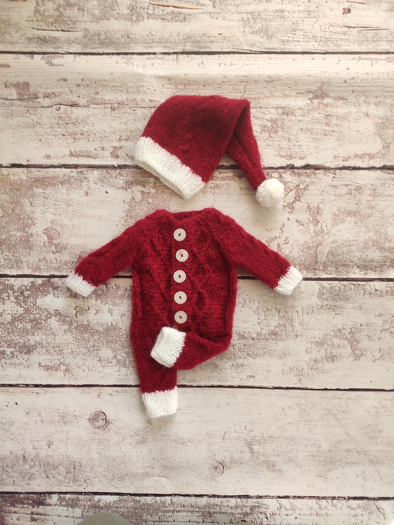 May include: Red knitted baby outfit with white trim and buttons, and a matching red knitted Santa hat with a white pom-pom.