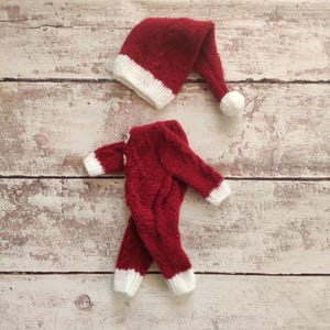 May include: Red knitted Santa suit with white trim for a newborn baby. The suit includes a matching hat with a white pom-pom.