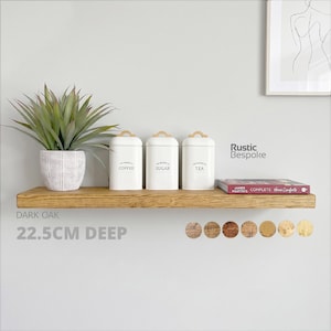 May include: A dark oak floating shelf measuring 22.5 cm deep, holding a potted green plant, three white canisters labeled Coffee, Sugar, and Tea, and a book titled James Martin's Complete Home Comforts. The text Rustic Bespoke is visible.