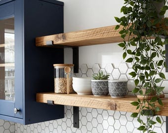 May include: Two natural wood floating shelves mounted with black metal brackets. The shelves hold a clear glass jar with a wooden spoon, white bowls, two patterned gray and white ceramic pots, and a trailing green plant in a gray pot.