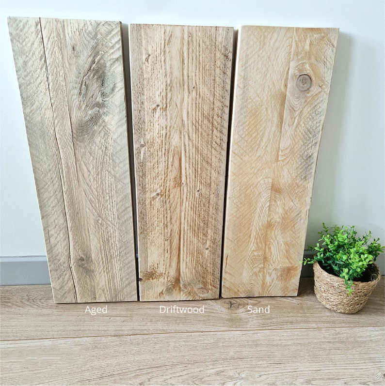 May include: Three wood samples, each with a different finish: aged, driftwood, and sand. The samples are arranged horizontally, with the aged sample on the left, the driftwood sample in the middle, and the sand sample on the right.