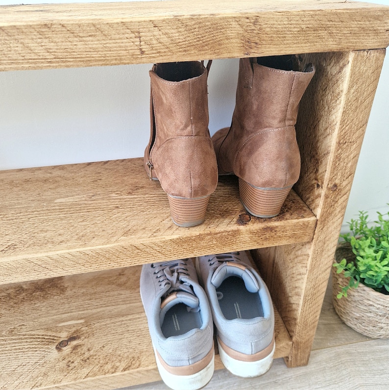 May include: A wooden shoe rack with two shelves. The top shelf has two pairs of brown ankle boots. The bottom shelf has two pairs of grey trainers.