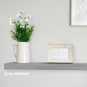 May include: A grey-washed wooden shelf displays a white pitcher with white flowers and a framed photo. The shelf is mounted on a light grey wall. The text "grey washed" is at the bottom of the shelf.