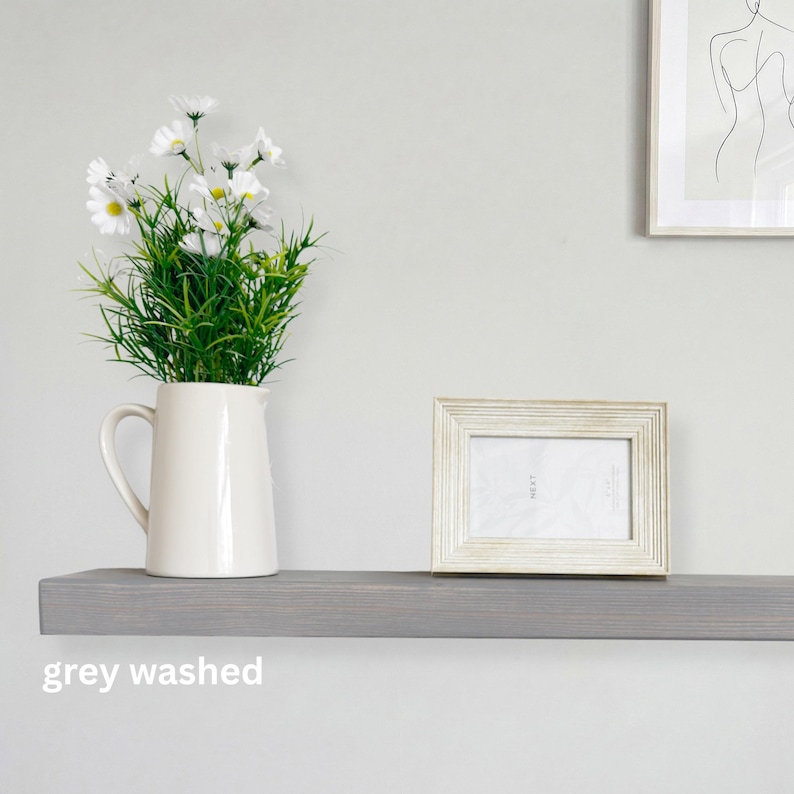 May include: A grey-washed wooden shelf displays a white pitcher with white flowers and a framed photo. The shelf is mounted on a light grey wall. The text "grey washed" is at the bottom of the shelf.