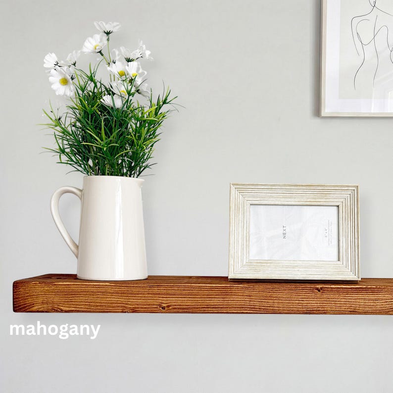 May include: A mahogany-colored wooden shelf with a white pitcher holding white daisies and green foliage. A white framed photo with the word "NEXT" is on the shelf. The word "mahogany" is at the bottom.