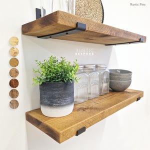 May include: Two rustic wooden shelves with black metal brackets. The shelves are mounted on a white wall and are decorated with a potted plant, glass jars, and bowls. The shelves are labeled "Rustic Bespoke".