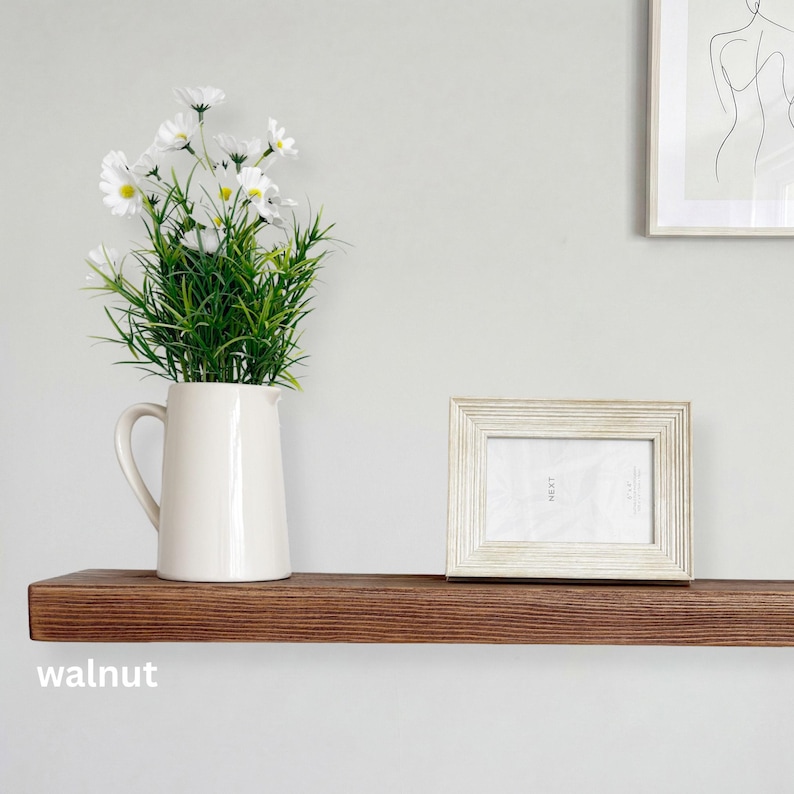 May include: A wooden shelf with a dark walnut finish, holding a white pitcher with white flowers and a white framed photo. The word "walnut" is printed on the shelf.