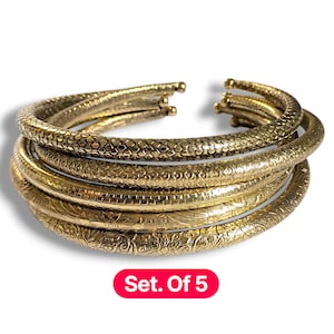 May include: A collection of five gold-coloured bangles with different embossed designs. The bangles have a textured finish and are arranged together. The text "Set. Of 5" is displayed in a red box.