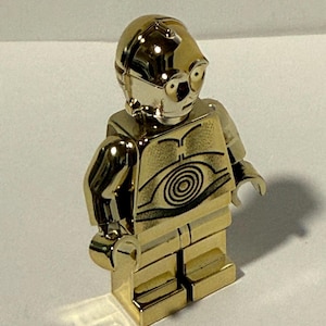 以下が含まれることがあります： スターウォーズのC-3POの金色のレゴフィギュア。このフィギュアはメタリックな仕上がりで、詳細なラインと胴体にある円形のデザインが特徴です。頭部は丸みを帯びており、目のディテールがあります。