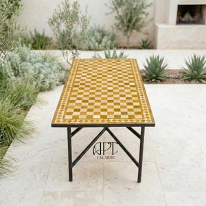 May include: A rectangular outdoor table with a mosaic tile top in shades of yellow and brown, set on a black metal frame. The table's top features a checkerboard pattern. The table is approximately 48 inches long.