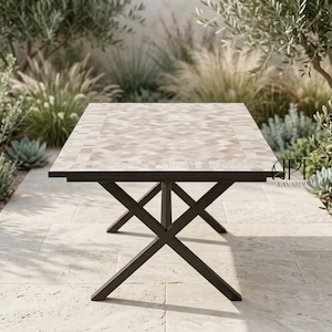Puede incluir: Mesa de comedor rectangular para exteriores con tablero de mosaico y patas de metal marrón oscuro. La superficie de la mesa tiene un patrón geométrico en beige claro. Las patas están cruzadas para mayor estabilidad. La mesa está rodeada de vegetación.