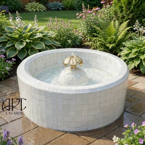 Puede incluir: Fuente redonda de mosaico blanco con un elemento acuático floral dorado. La fuente está llena de agua y se encuentra sobre un patio de ladrillos, rodeada de vegetación y flores. El texto "ART LAVARDE" es visible.
