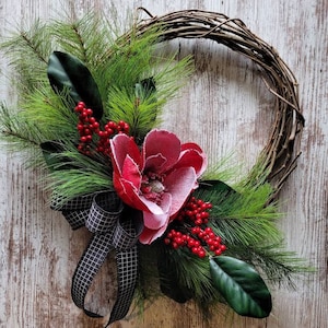 Christmas front door wreath with red flocked magnolia, pine needles, red berries, and plaid black and white farmhouse  ribbon for your porch
