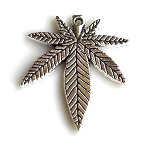 May include: Silver charm in the shape of a marijuana leaf. The leaf has a detailed design with a textured surface.