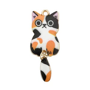 May include: A colorful cat charm with a gold-tone metal frame. The cat has a white body with orange and black spots, a black and orange tail, and a pink and black head. The charm is designed to be used as a pendant or a decorative element.