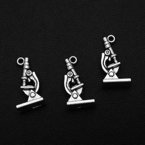 May include: Three silver microscope charms with a loop for hanging. The charms are detailed and have a vintage look.