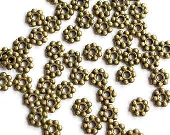 May include: A scattering of antique gold metal beads with a flower design. Each bead has a small hole in the center.