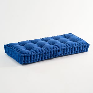 May include: A rectangular, tufted cushion in a vibrant blue hue. The cushion features a series of evenly spaced, raised squares across its surface. The edges are finished with a decorative, ruffled trim. A handle is visible on one side.