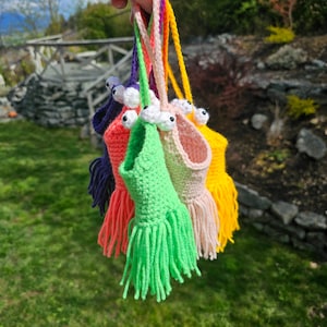 May include: Five crocheted finger puppets with googly eyes and fringe. The puppets are in various colours, including green, pink, orange, and yellow.