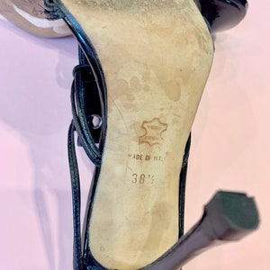 May include: Black leather high-heeled sandals with a buckle closure and a strap across the foot. The sandals are made in Italy and are size 38 1/2.